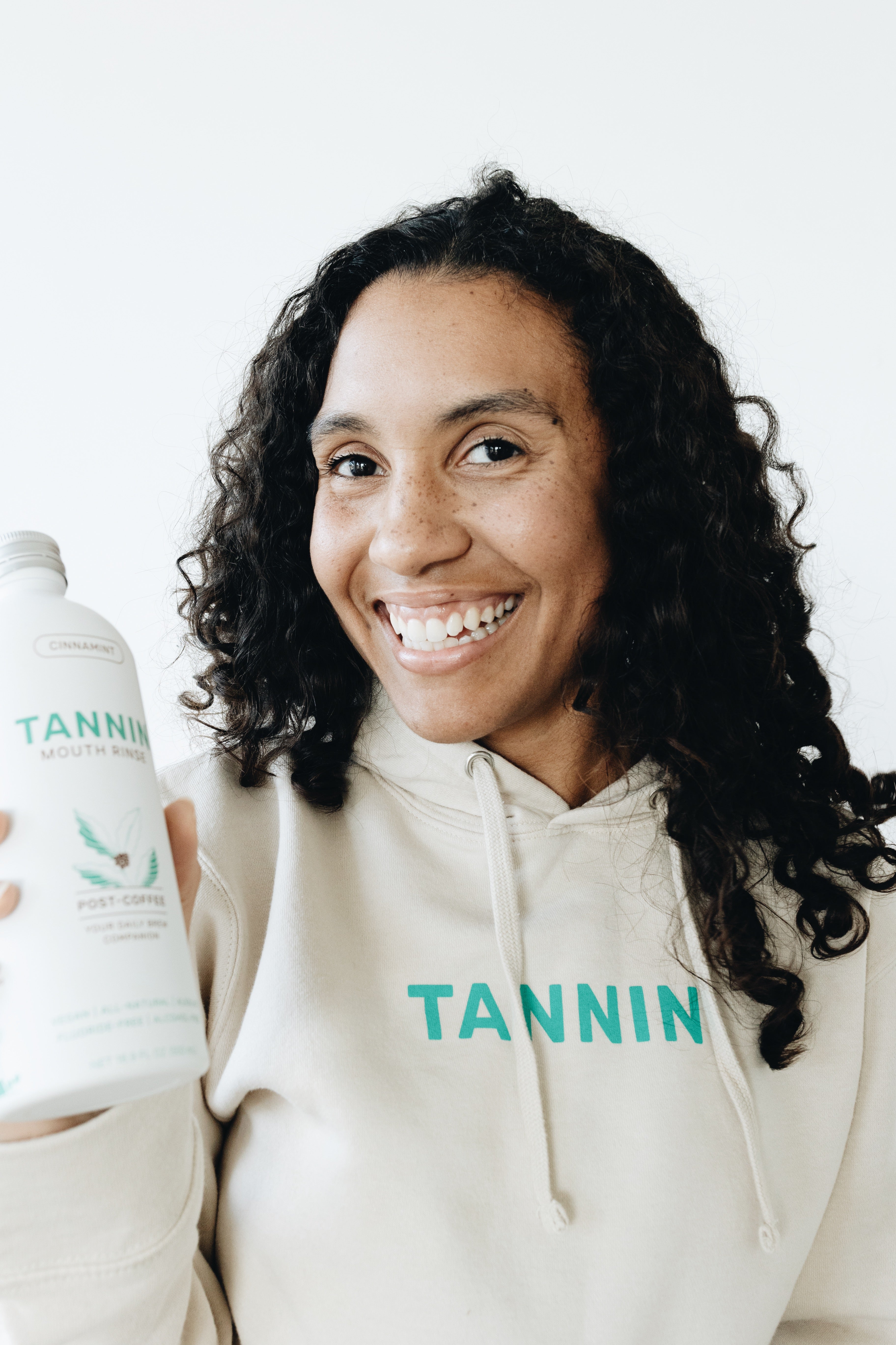 Woman smiling confidently while holding a Tannin mouth rinse bottle, representing the brand’s commitment to empowering individuals to feel their best.