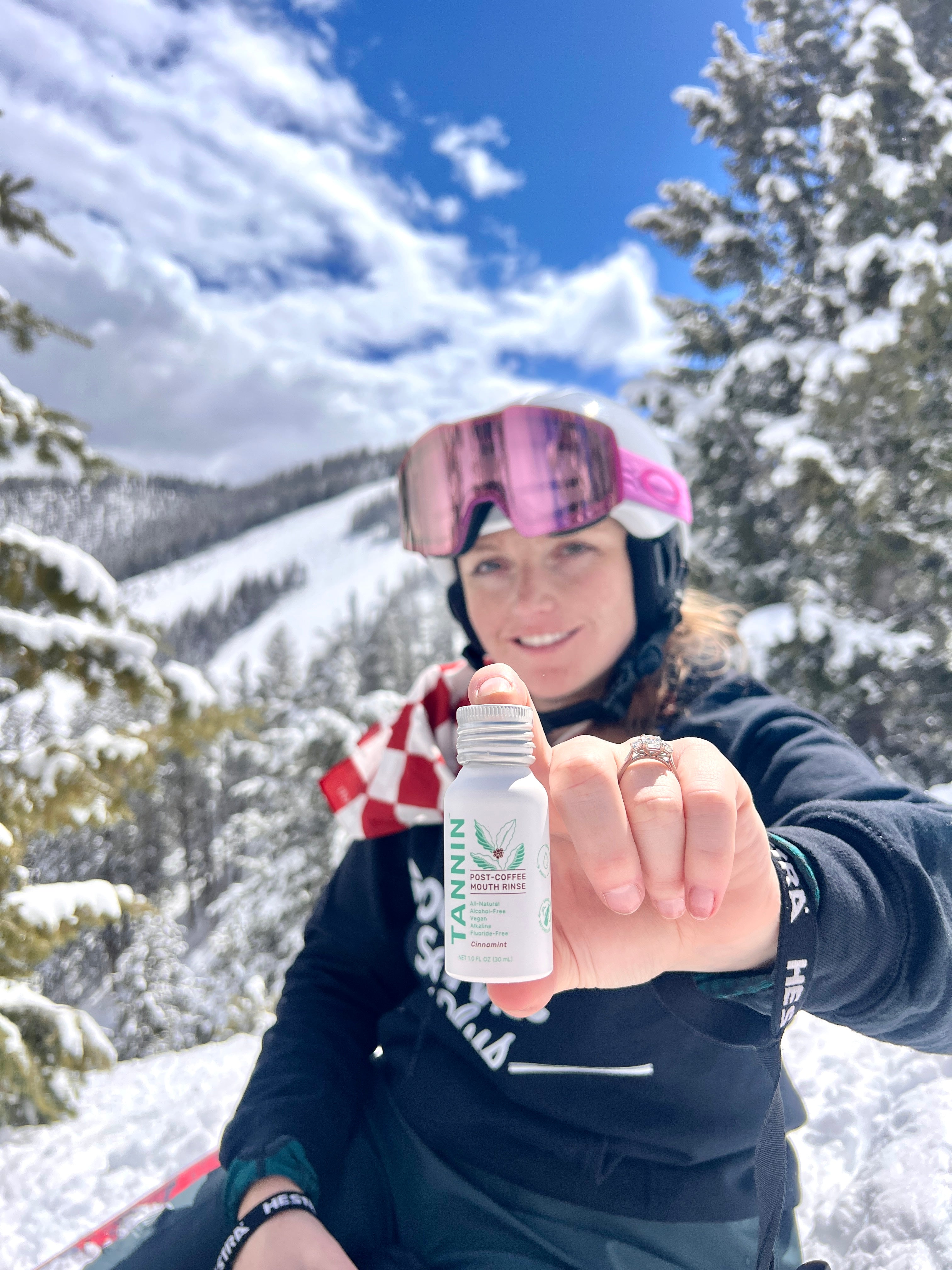 Woman holding a small bottle outdoors with snowy landscape and trees in the background.