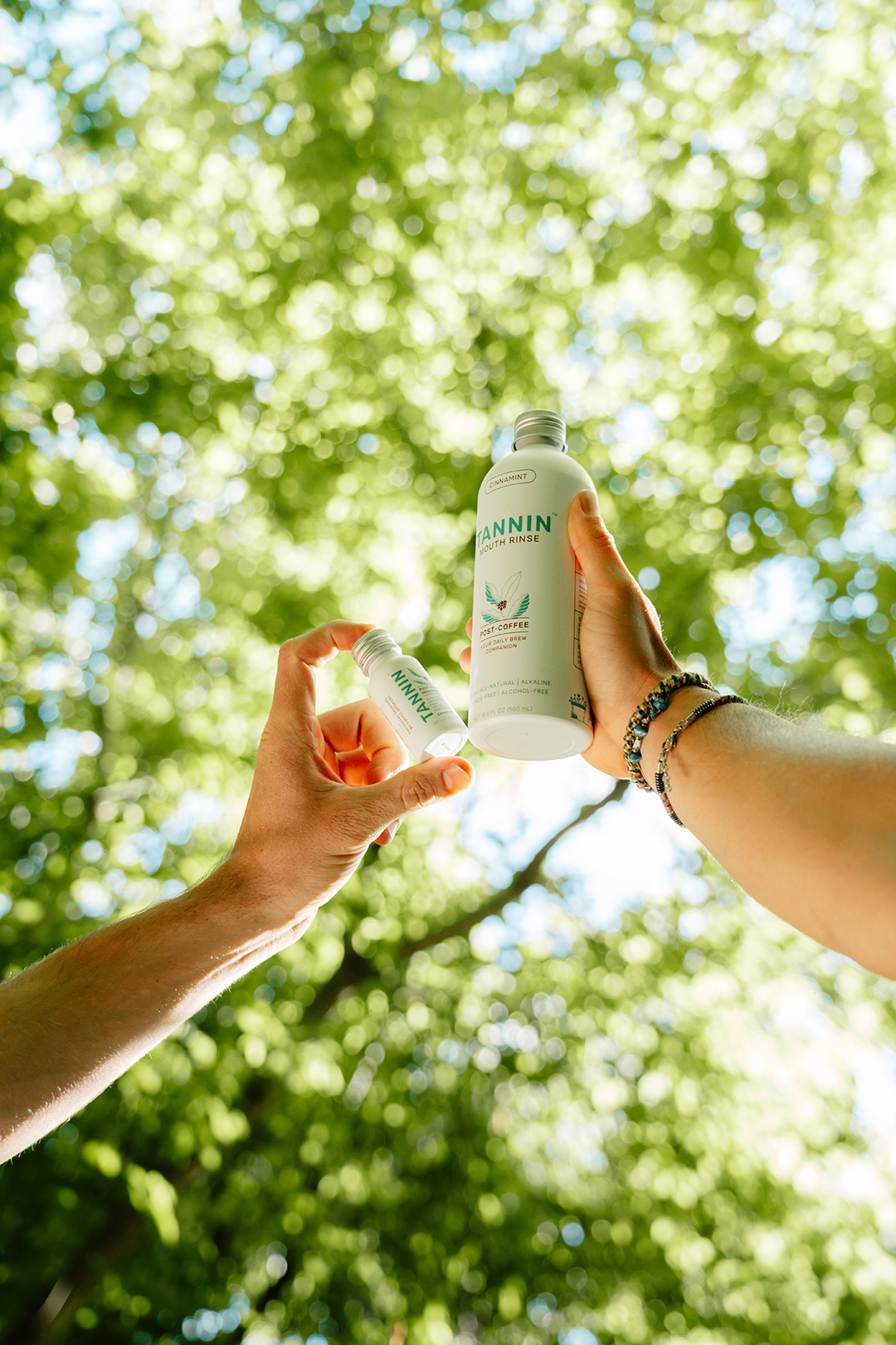 Hand holding a Tannin rinse bottle with greenery in the background, showing the first step: shake well, as natural separation occurs.