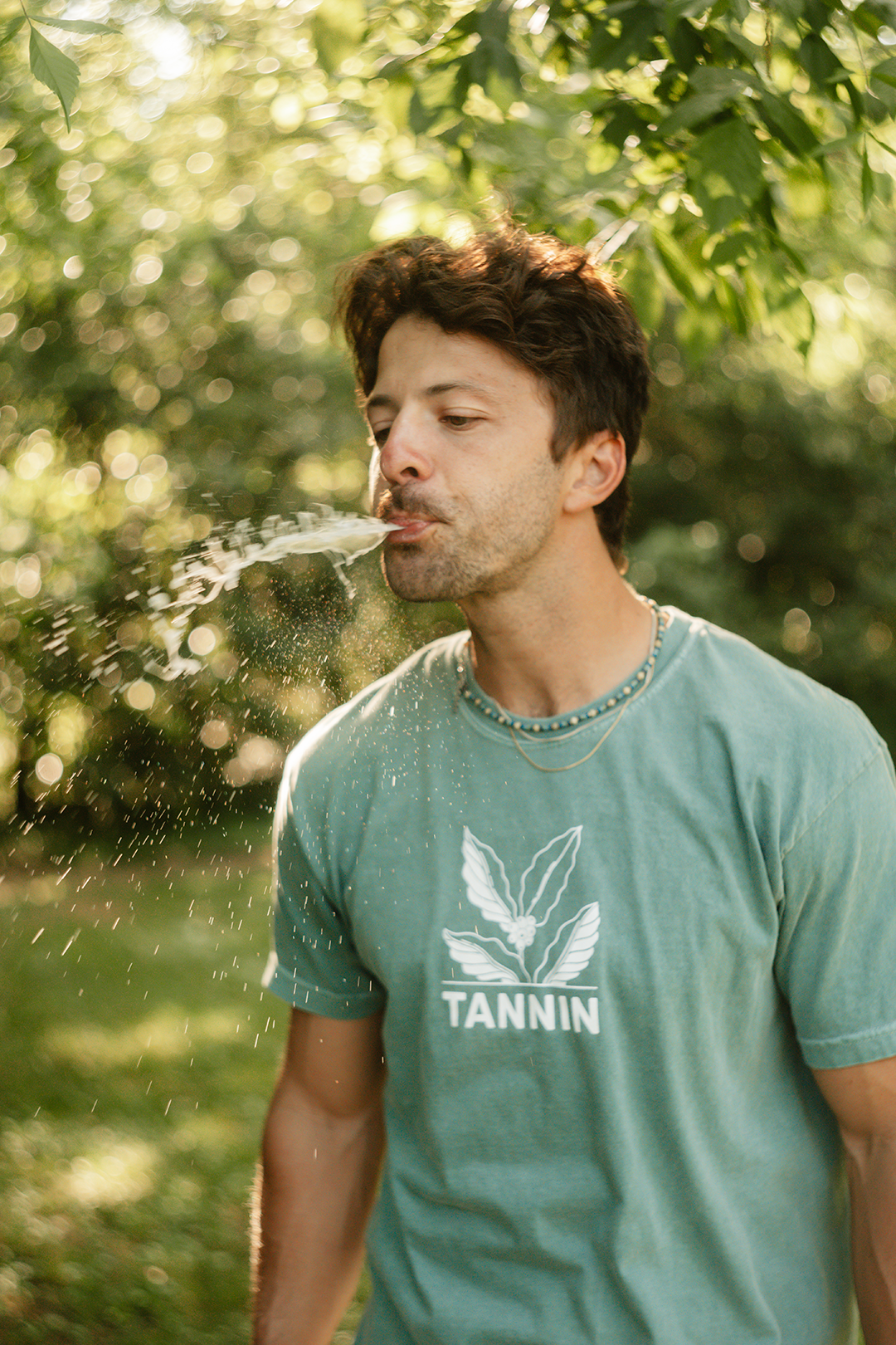 Man in a Tannin shirt spitting out the rinse in a natural setting, completing the third step: spit, with a playful reminder to &#39;not make it weird.