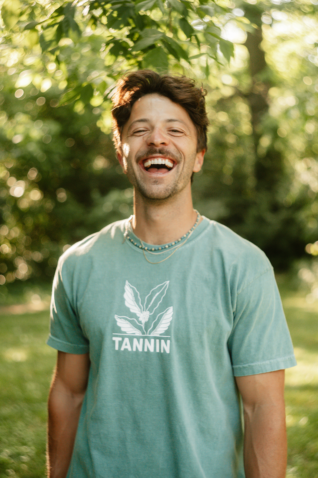 Man smiling broadly in a Tannin shirt, showing off his clean teeth after completing the final step: share your smile with confidence.