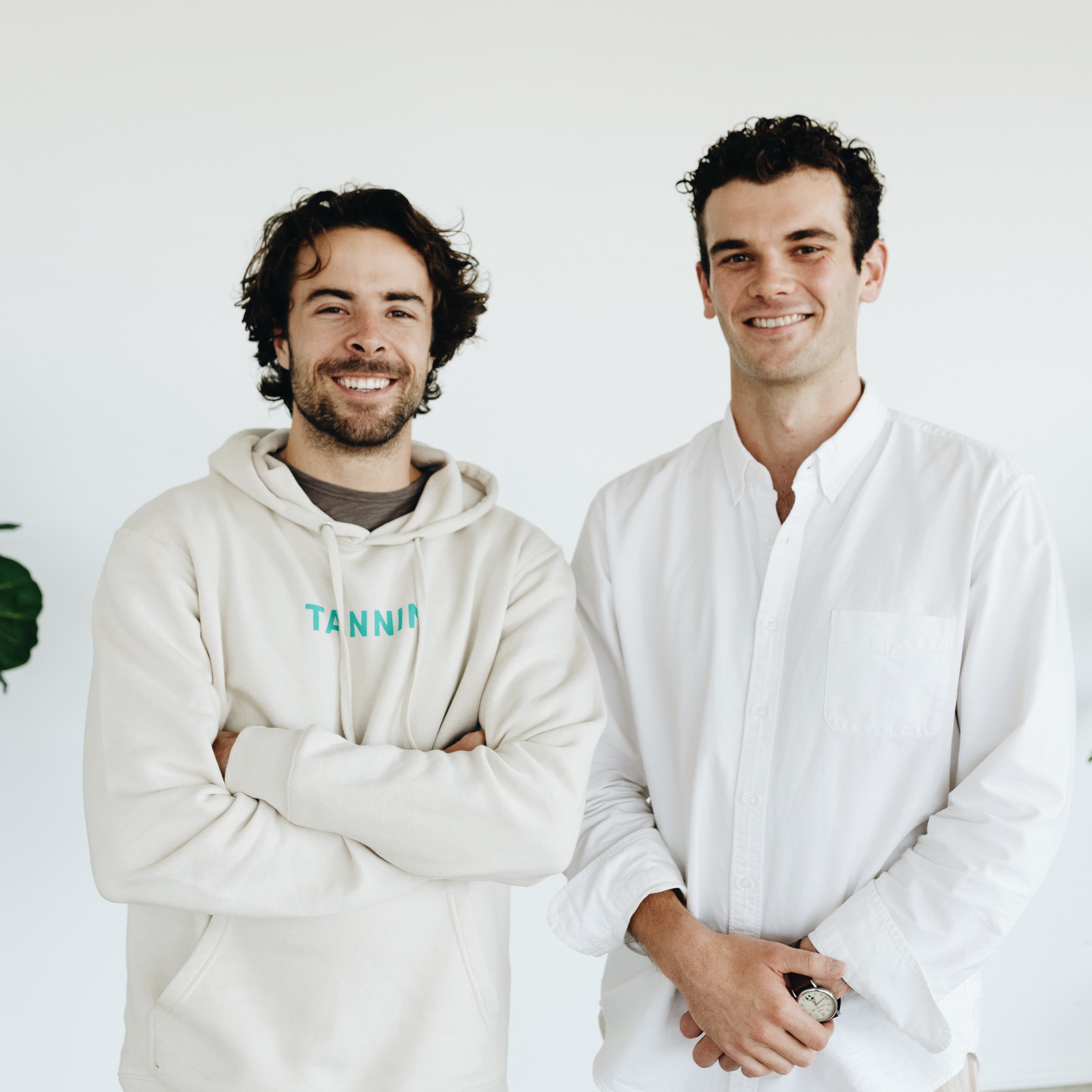 Tannin co-founders Joe and Henry smiling indoors. Henry wears a Tannin hoodie, while Joe wears a white shirt, symbolizing the teamwork and vision behind the brand.