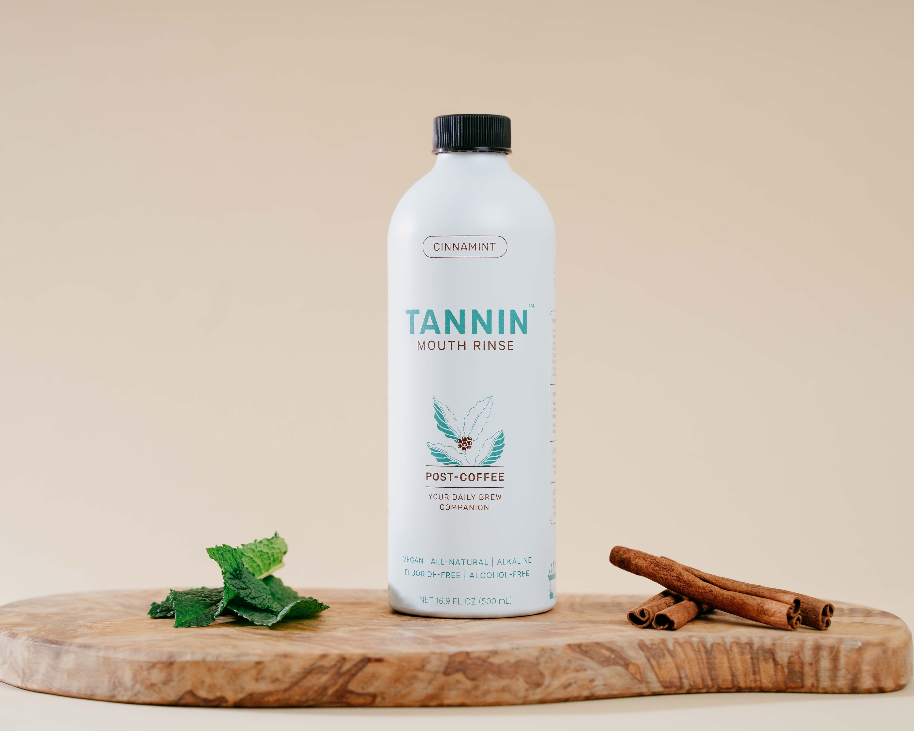 Tannin Post-Coffee Mouth Rinse bottle on a wooden board with mint leaves and cinnamon sticks, highlighting an all-natural, alcohol-free solution for combating coffee breath and improving oral health.